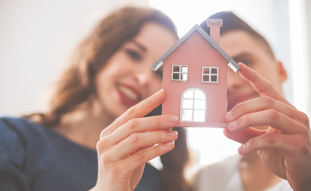 Happy couple holding a model home, envisioning their new home construction in New Orleans with NOLA Build.