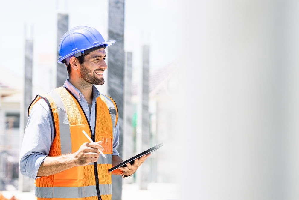 Chief engineer in a hard hat navigating through a modern factory with a laptop, depicting professionalism in an industrial setting.