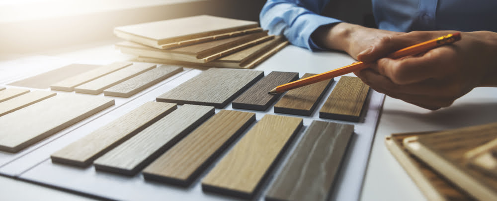 Wood texture furniture material samples for interior design, with a designer working at a desk in a New Orleans construction company office.